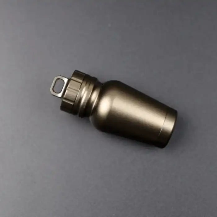 Aluminum pill case with bronze finish laying flat on a dark surface showcasing its compact cylindrical design.