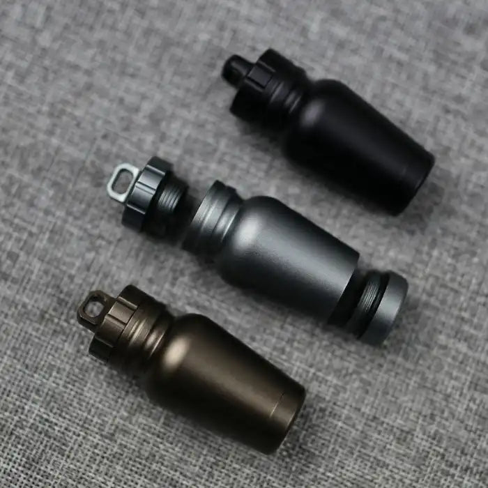 Trio of aluminum pill cases in black, grey, and bronze colors shown open on textured fabric surface.