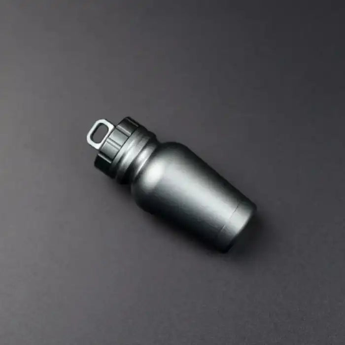 Gunmetal black aluminum pill case with looped lid placed on black background for sleek industrial look.