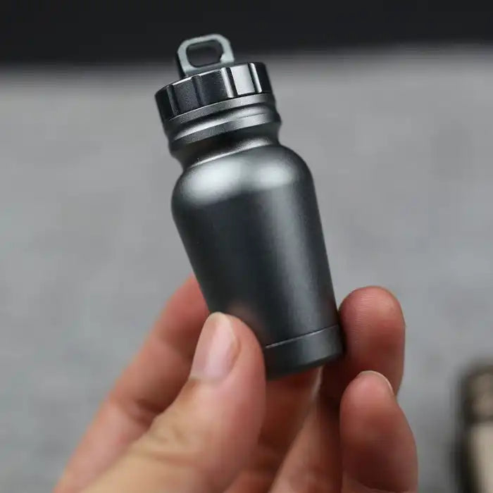 Aluminum pill case in matte grey held in hand with a secure twist cap and keyring loop for portability.