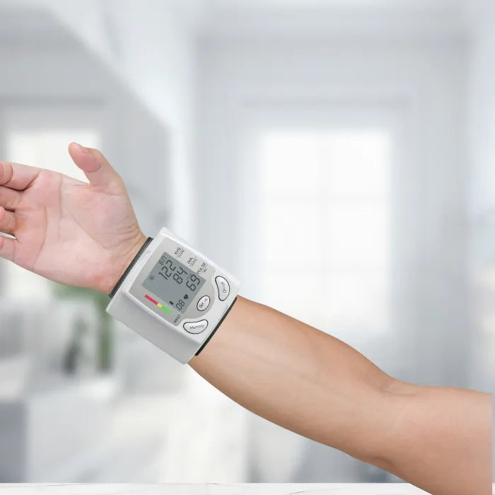 Blood pressure tester wrapped around wrist in use, displaying digital reading on screen.