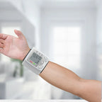 Blood pressure tester wrapped around wrist in use, displaying digital reading on screen.