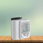 Wrist blood pressure tester standing upright on wooden surface with green gradient background.