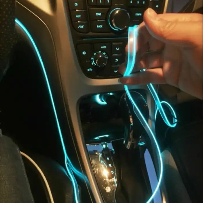 Blue car LED light strip being installed along dashboard and gear shift panel by hand