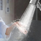 High pressure shower head spraying strong water stream onto a hand in close-up.