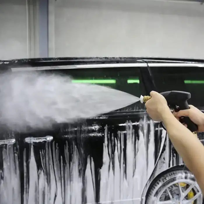 Pressure washer spraying thick foam on black vehicle during car wash using white tip nozzle