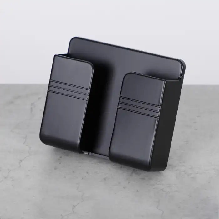 Black wall mount phone holder with smooth matte finish placed on gray stone surface