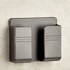Metallic black wall mount phone holder mounted on textured surface with minimalist dual-clip design.